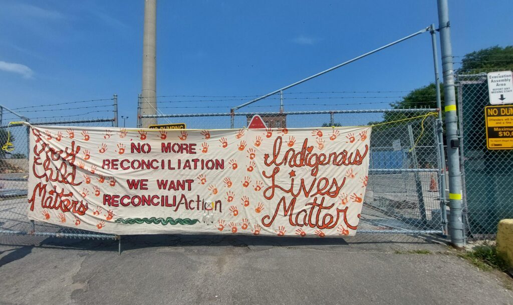 Photo: Large canvas banner that reads No More Reconciliation. We Want Reconcili-Action. Indigenous Lives Matter